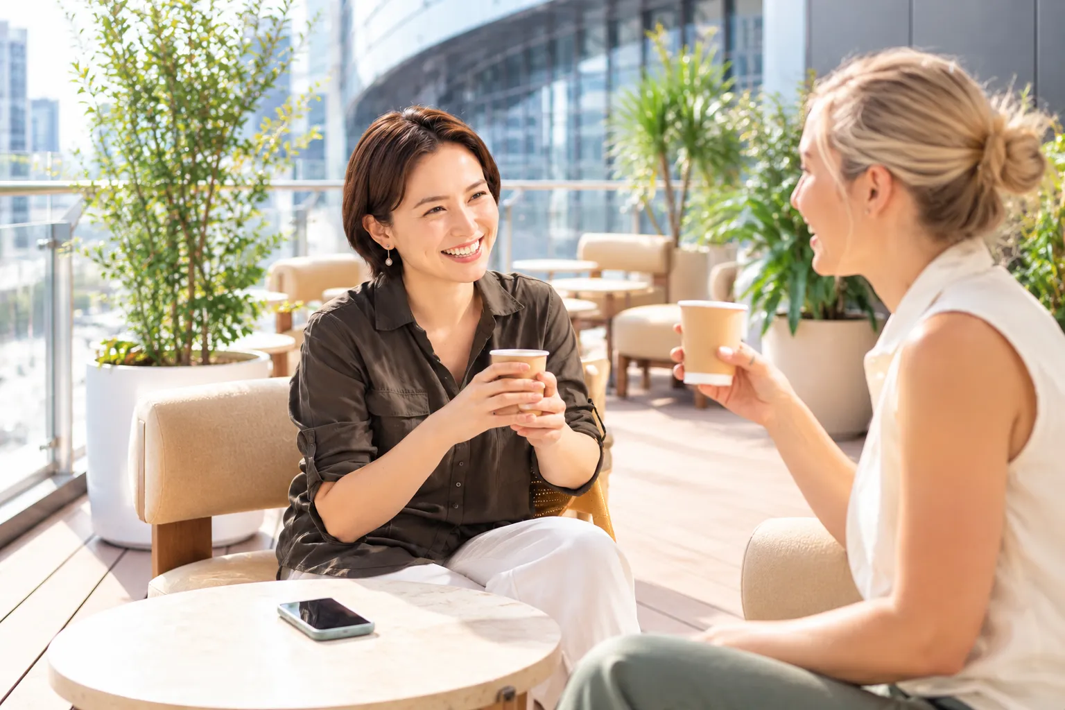明るいテラスカフェでコーヒーを飲みながら会話する二人の女性